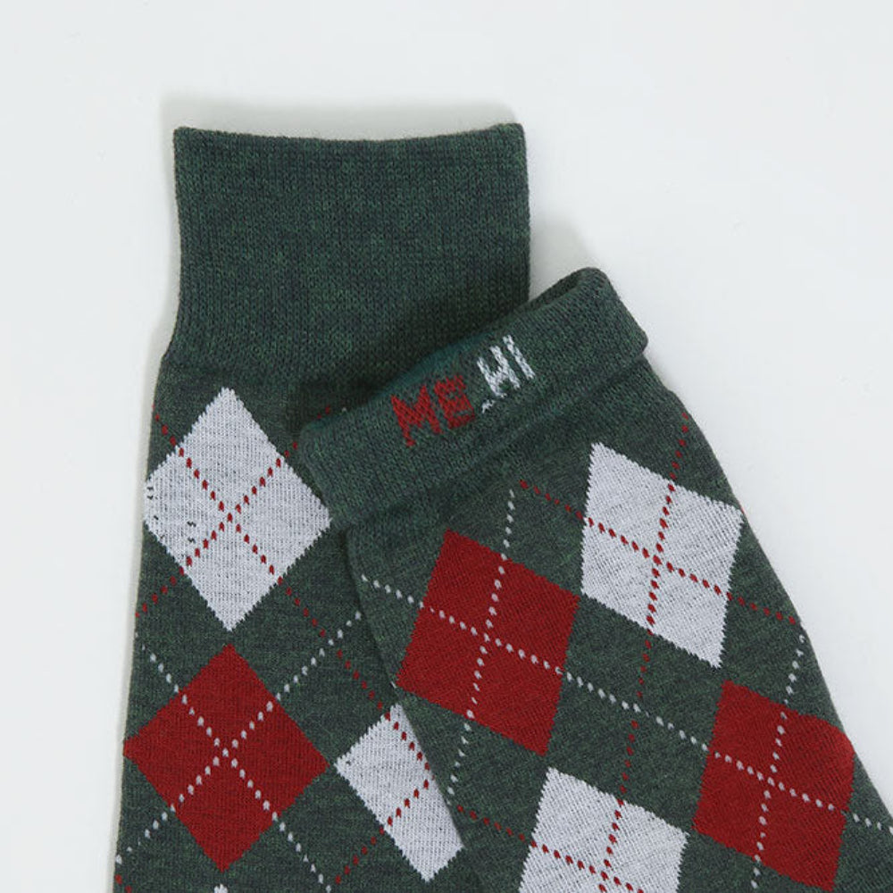 A close-up of a folded knit garment, likely a sweater or scarf, in dark green with an argyle pattern in red and white, featuring a small red and white embroidered logo on the cuff.