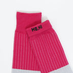 A pair of bright pink crew socks with thin white pinstripes, featuring a black embroidered 'ME,HI' logo on the cuff and a light gray ribbed toe section, displayed on a clean white background.
