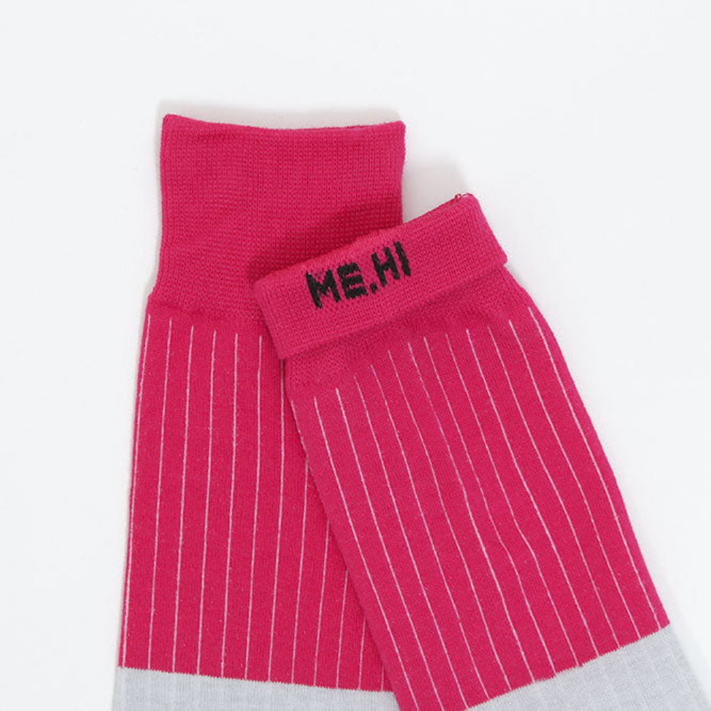 A pair of bright pink crew socks with thin white pinstripes, featuring a black embroidered 'ME,HI' logo on the cuff and a light gray ribbed toe section, displayed on a clean white background.