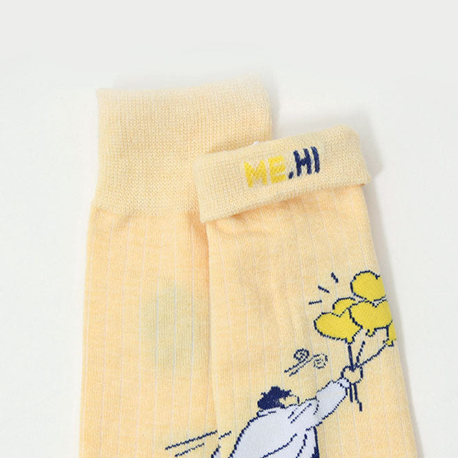 A pair of pale yellow crew socks with a cartoon graphic of a person holding yellow balloons and the text 'ME, HI' on the cuff, shown against a plain white background.