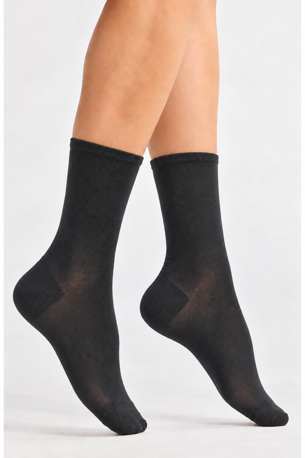 A pair of black crew socks worn on a model's feet, shown against a plain light gray studio background.