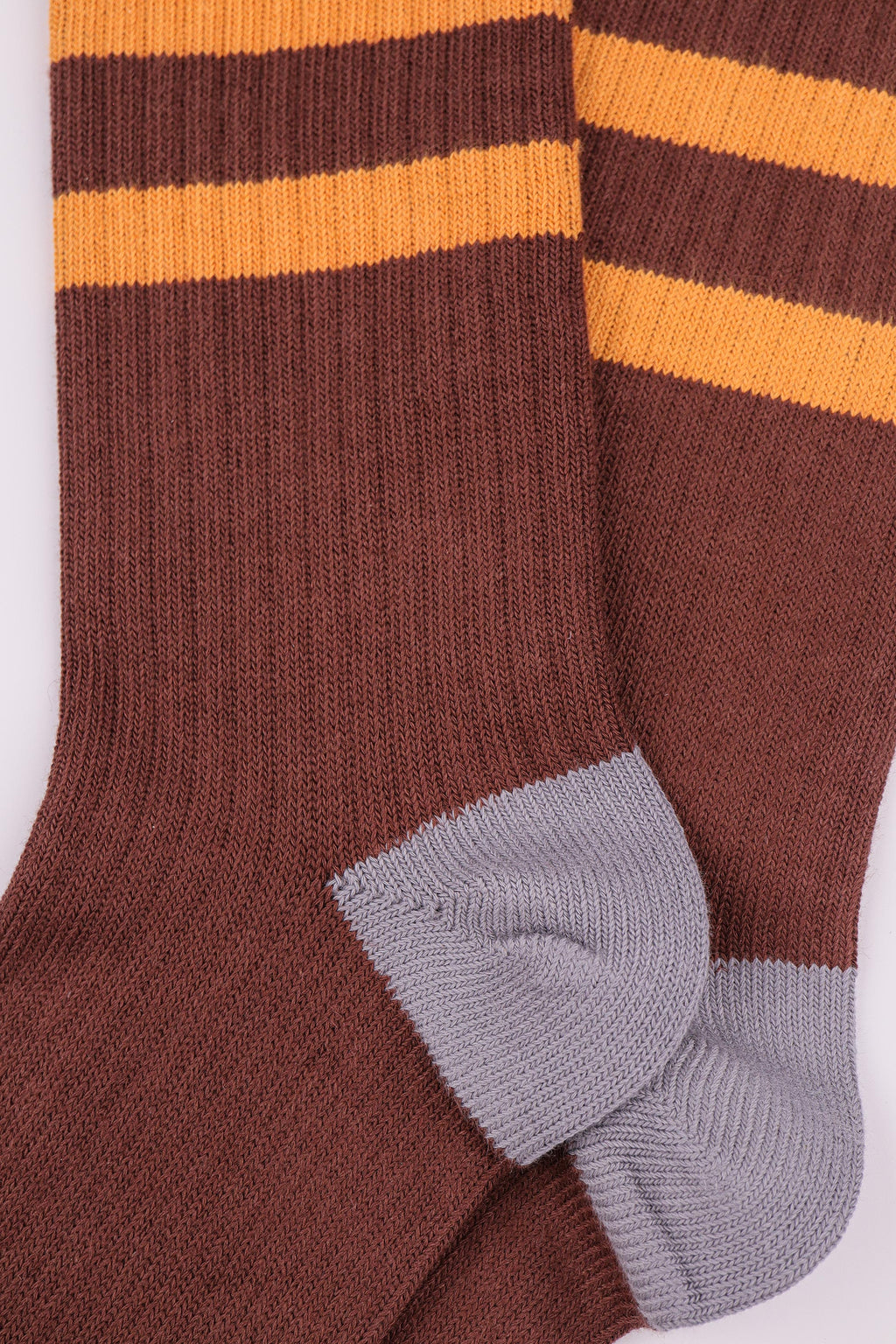 A close-up of a pair of ribbed knit socks in dark brown with two horizontal yellow stripes near the top and light gray heels and toes, shown on a plain white background.