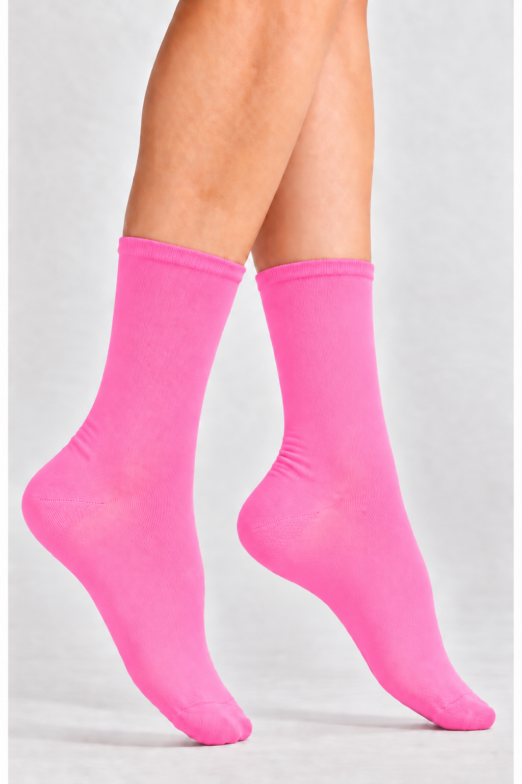 A person seated wearing bright pink crew socks and a white dress with black polka dots, photographed against a light gray studio background.